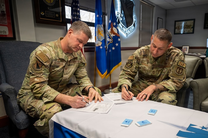 Col Richards and Chief Master Sergeant Serrano sit at a table and each sign their AFAF pledge form.