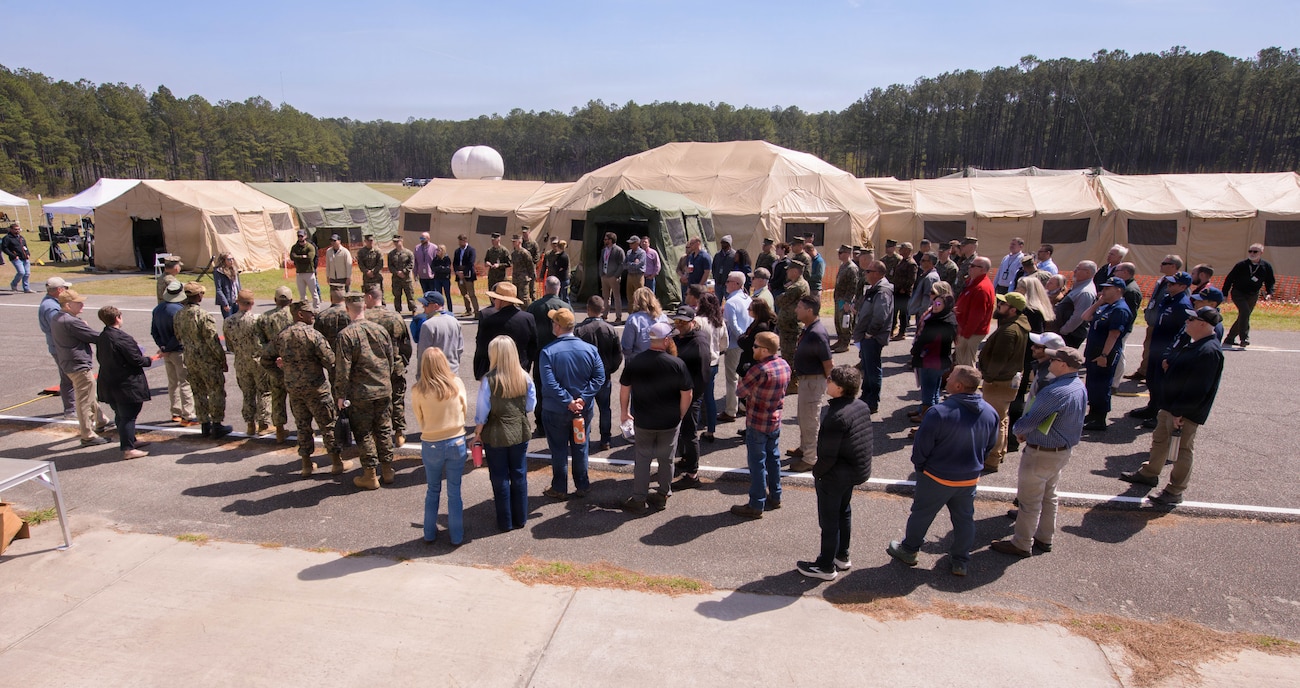 Military personnel and civilians gather around a table inside a portable shelter to collaborate on digital systems and mission threads during the SoSNIE experiment.