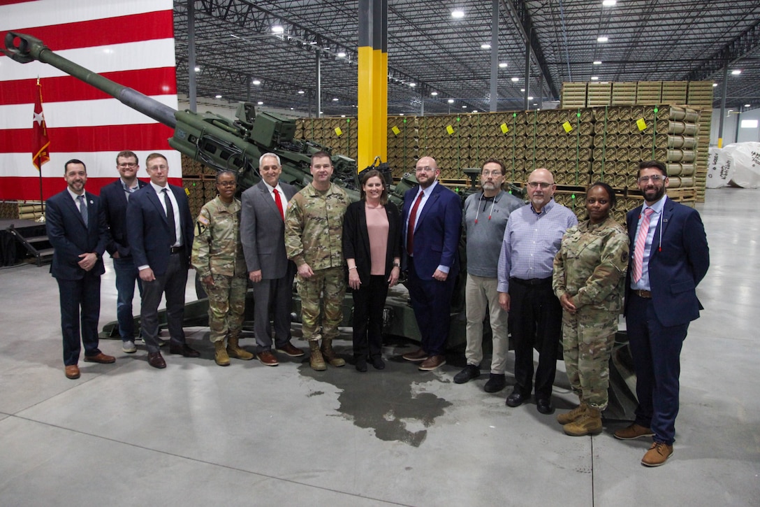 A group of military personnel and civilians stand near a flag