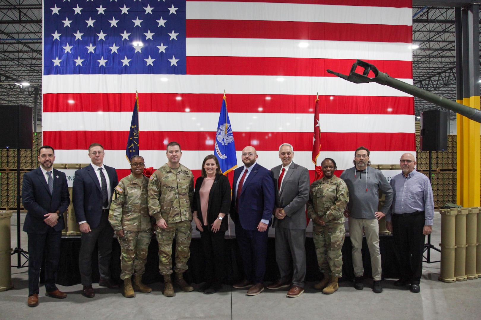 A group of military personnel and civilians stand in front of a flag