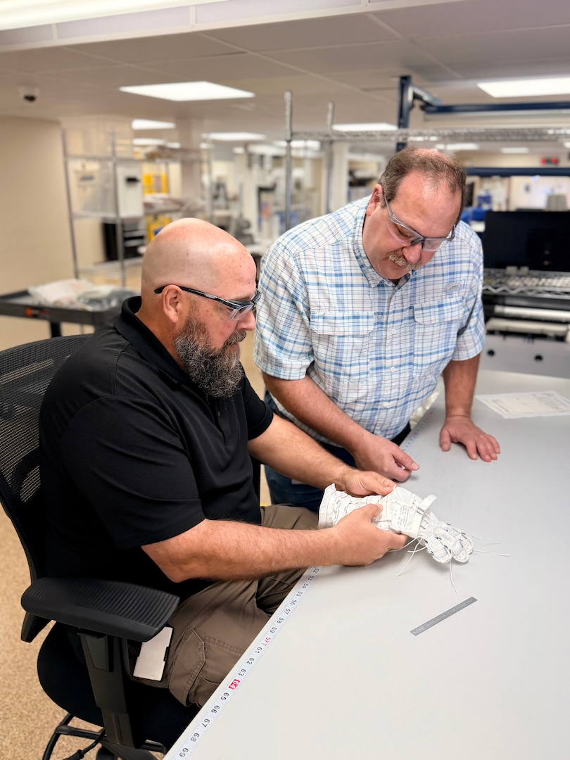 Two men look at stitching on a glove.