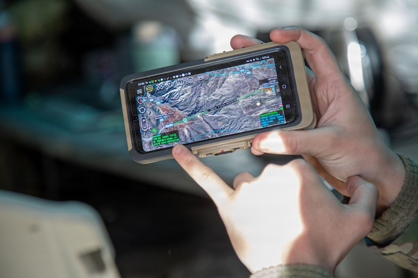 A close-up view of a person holding a handheld device depicting terrain, coordinates and other information.