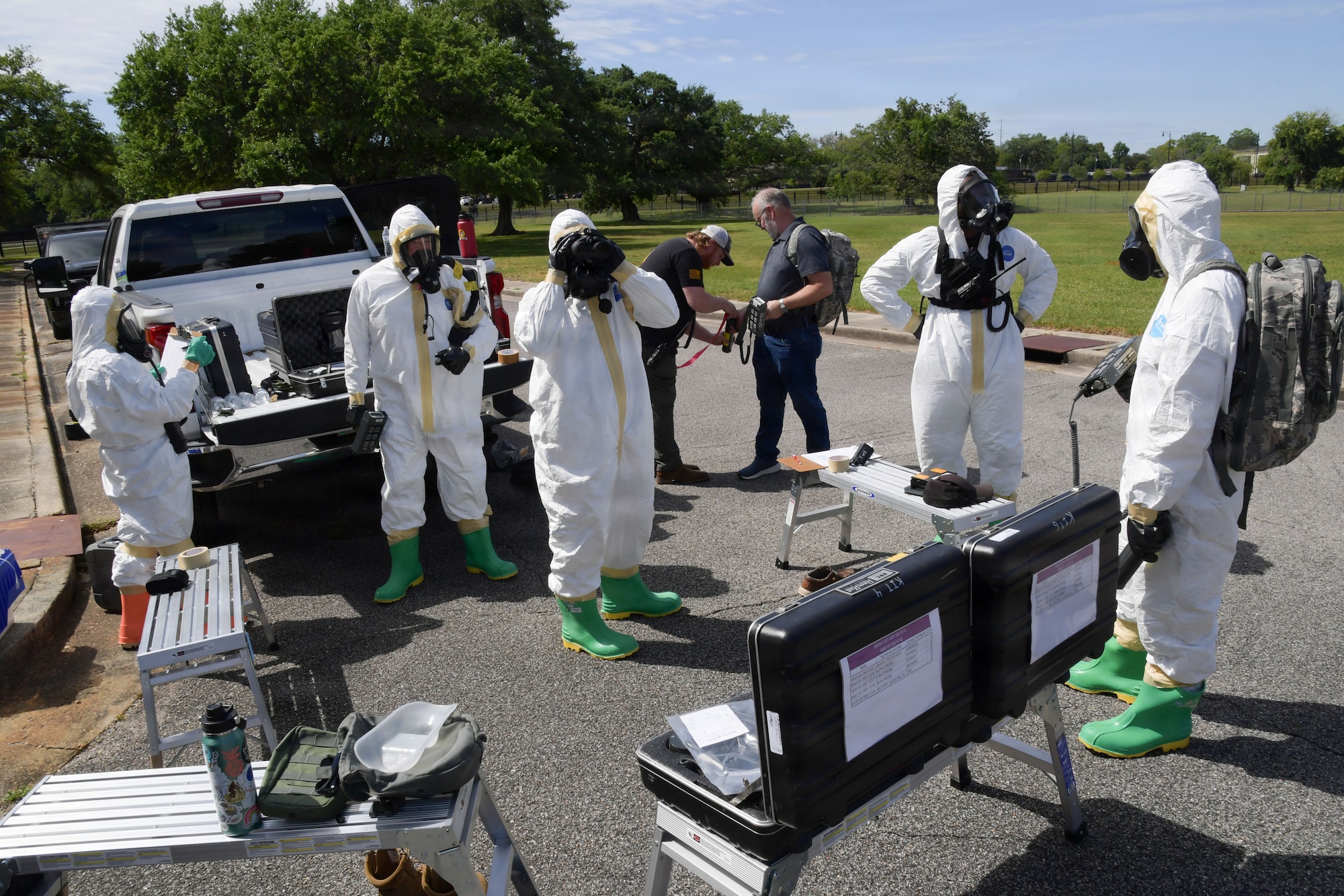 A group of people in white hazmat uniforms gather together with equipment.