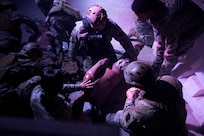 Servicemembers crouching down and surrounding a patient in a medevac exercise.