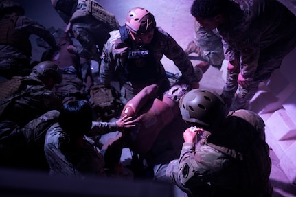 Servicemembers crouching down and surrounding a patient in a medevac exercise.