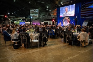 Group of people seated at round tables looking at a screen.