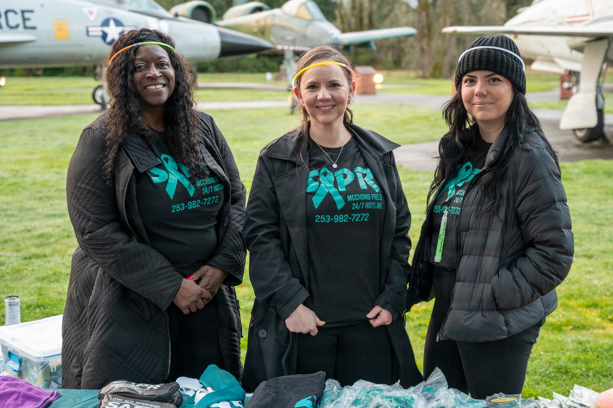 Cynthia Forsyth, 62d Airlift Wing Sexual Assault Prevention and Response victim advocate, left, Samantha Robertson, 62d AW SAPR Program Manager, center, and Ivey Sanchez, 62d AW SAPR victim advocate, stand together during the Sexual Assault Awareness and Prevention Month Glow Run 5K at Joint Base Lewis-McChord, Washington, April 2, 2025.