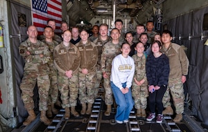 Air Force service members and ROTC cadets stand for a group photo inside a C-130H Hercules aircraft.