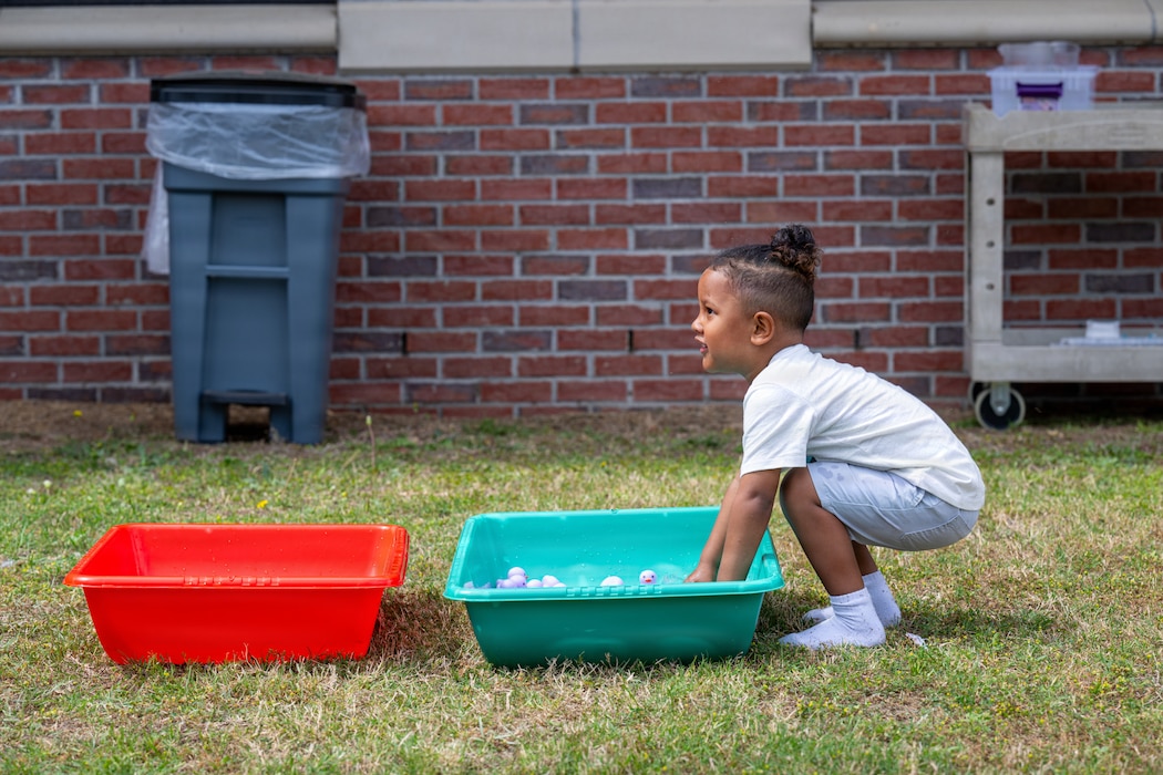 A child plays with a bucket of water with rubber ducks in it.