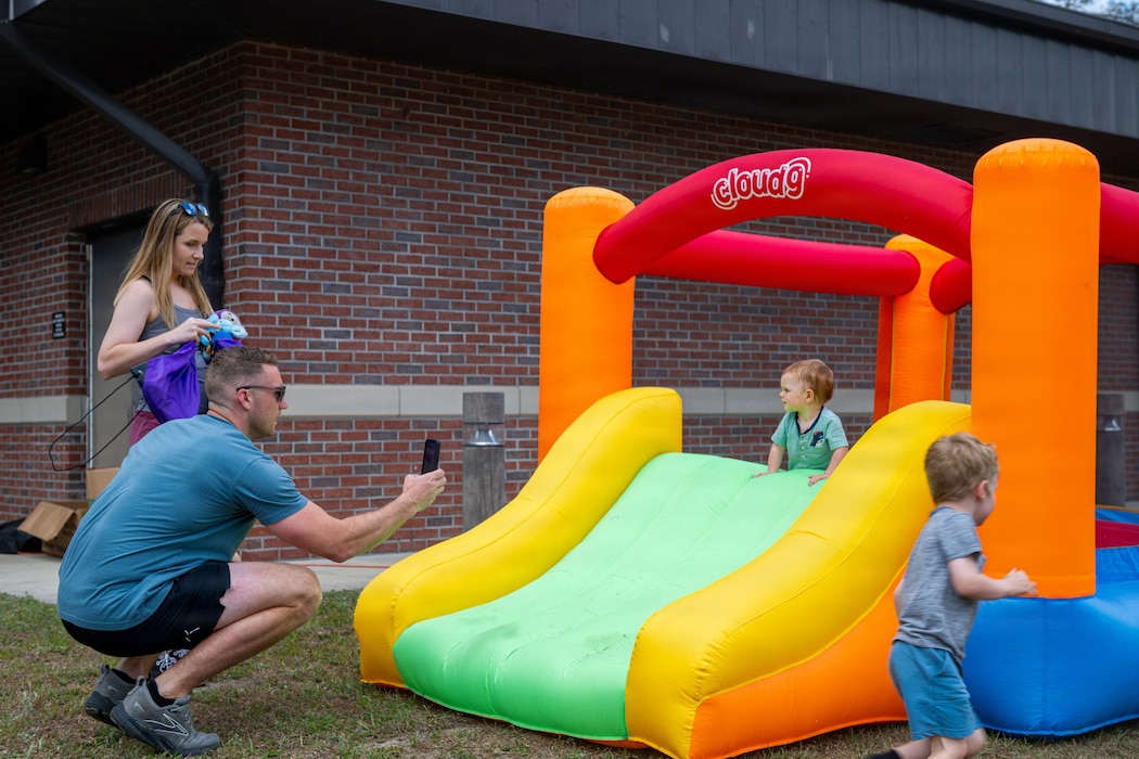 Two kids play on a bouncy house while mother and father take photos.