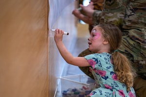 Kid drawing on a piece of paper on the wall.