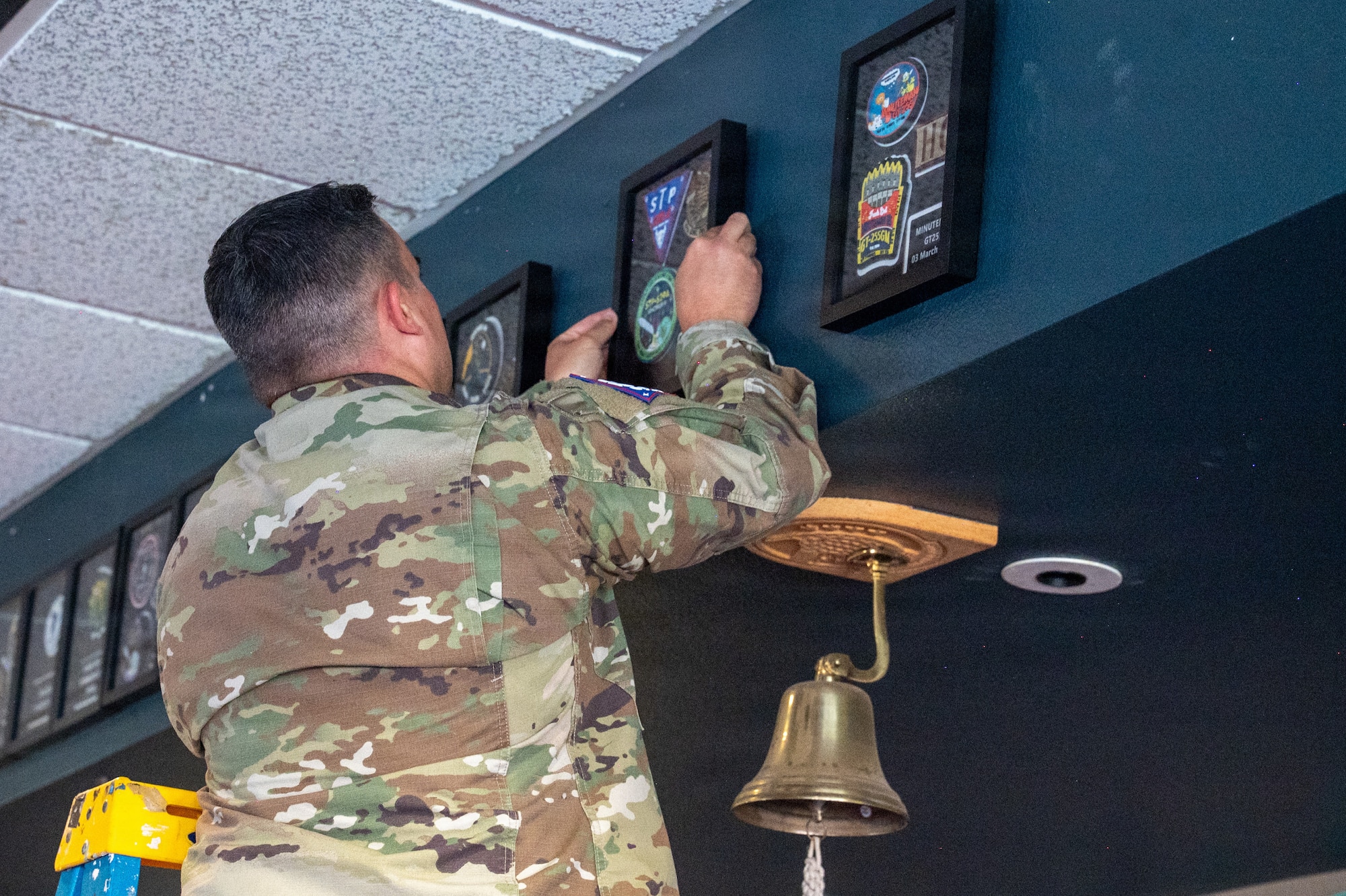 U.S. Space Force Lt. Col. Ralph Salazar hangs framed patches on a wall.