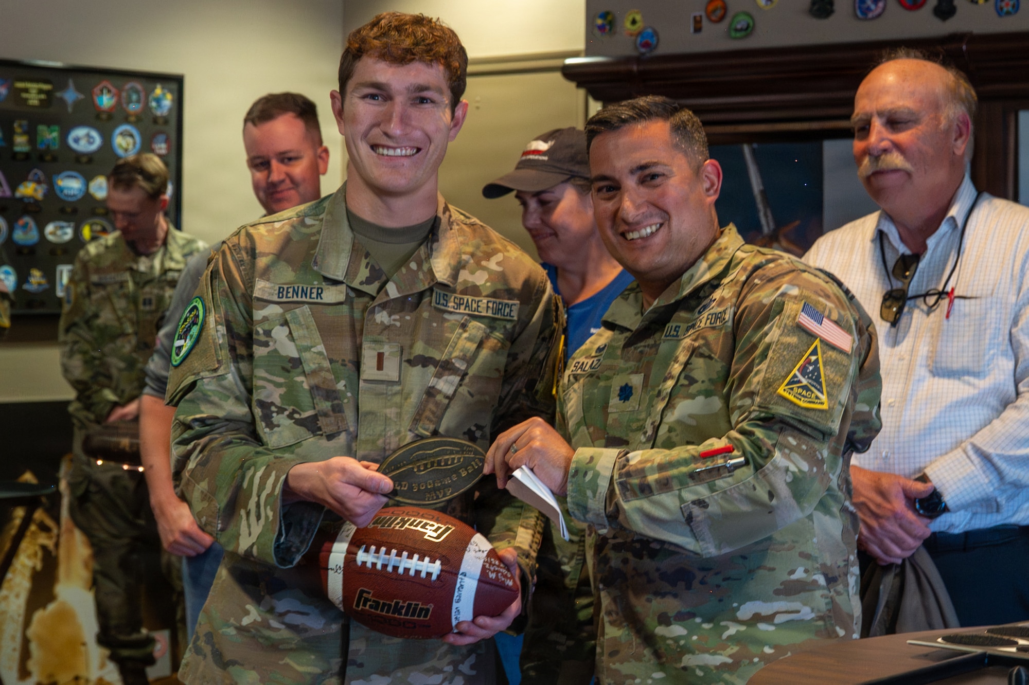 U.S. Space Force Lt. Col. Ralph Salazar hands the ceremonial game ball to 2nd Lt. Zachery Benner and they smile for a photo.