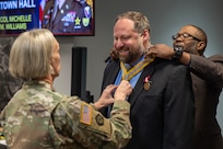 Col. Michelle M. Williams, U.S. Army Financial Management Command commander, left, and Retired Command Sgt. Maj. Gennaro Penn, U.S. Army Finance Corps Association president, right, present Ryan A. Busby, Deputy Assistant Secretary of the Army for Financial Operations and Information, with a U.S. Army Finance Corps’ Honorary Member of the Regiment award on behalf of Col. Robert Le'iato, U.S. Army Finance and Comptroller School commandant and Chief of the Finance Corps, at the Maj. Gen. Emmett J. Bean Federal Center in Indianapolis Jan. 12, 2026. The Finance Corps designated the first Honorary Member of the Regiment on July 5, 1988, to honor those who made significant professional contributions or have brought great credit to the Finance Corps through special acts or accomplishments. (U.S. Army photo by Mark R. W. Orders-Woempner)