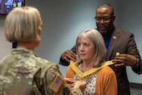 Col. Michelle M. Williams, U.S. Army Financial Management Command commander, left, and Retired Command Sgt. Maj. Gennaro Penn, U.S. Army Finance Corps Association president, right, present Valerie Dillon, USAFMCOM secretary to the general staff, with a U.S. Army Finance Corps’ Honorary Member of the Regiment award on behalf of Col. Robert Le'iato, U.S. Army Finance and Comptroller School commandant and Chief of the Finance Corps, at the Maj. Gen. Emmett J. Bean Federal Center in Indianapolis Jan. 12, 2026. The Finance Corps designated the first Honorary Member of the Regiment on July 5, 1988, to honor those who made significant professional contributions or have brought great credit to the Finance Corps through special acts or accomplishments. (U.S. Army photo by Mark R. W. Orders-Woempner)