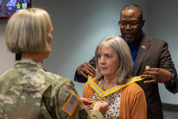 Col. Michelle M. Williams, U.S. Army Financial Management Command commander, left, and Retired Command Sgt. Maj. Gennaro Penn, U.S. Army Finance Corps Association president, right, present Valerie Dillon, USAFMCOM secretary to the general staff, with a U.S. Army Finance Corps’ Honorary Member of the Regiment award on behalf of Col. Robert Le'iato, U.S. Army Finance and Comptroller School commandant and Chief of the Finance Corps, at the Maj. Gen. Emmett J. Bean Federal Center in Indianapolis Jan. 12, 2026. The Finance Corps designated the first Honorary Member of the Regiment on July 5, 1988, to honor those who made significant professional contributions or have brought great credit to the Finance Corps through special acts or accomplishments. (U.S. Army photo by Mark R. W. Orders-Woempner)