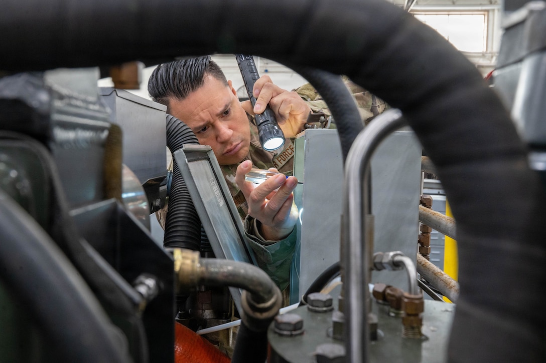 An airman uses a flashlight and screwdriver to work on a nitrogen cart in a maintenance room.
