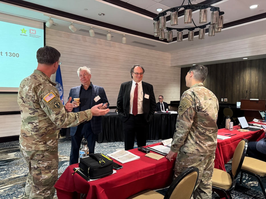 2 men in uniforms talk to 2 men in suits