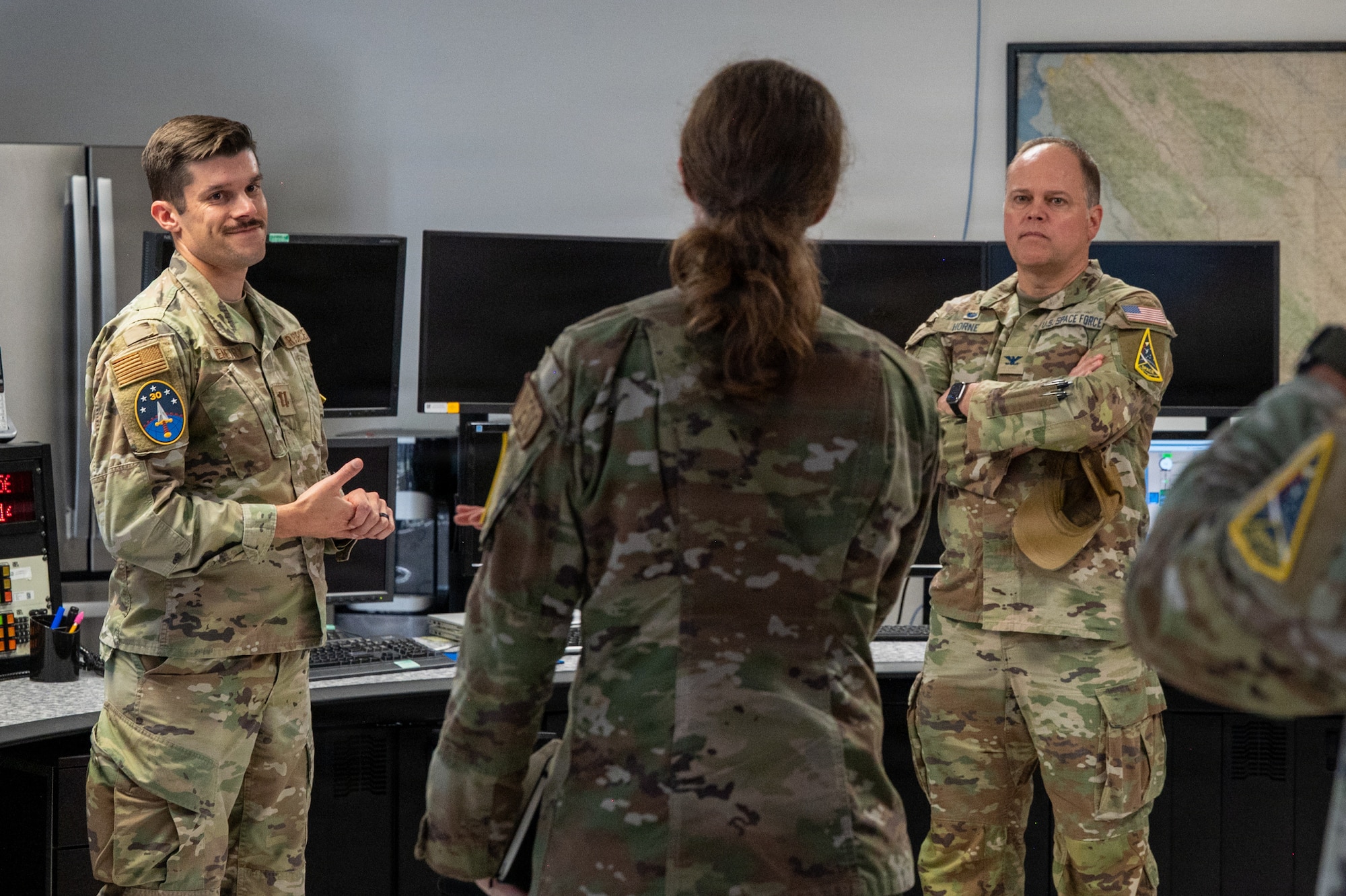 U.S. Space Force Col. James T. Horne III, right, Space Launch Delta 30 commander, stands and listens to a briefing. Two weather facility operators stand near him.