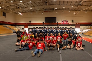 JROTC students pose for a group photo sitting in front of the standing Air Force Honor Guard Drill Team.