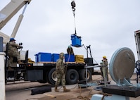 Airmen guide a replacement battery into a launch facility using a crane.
