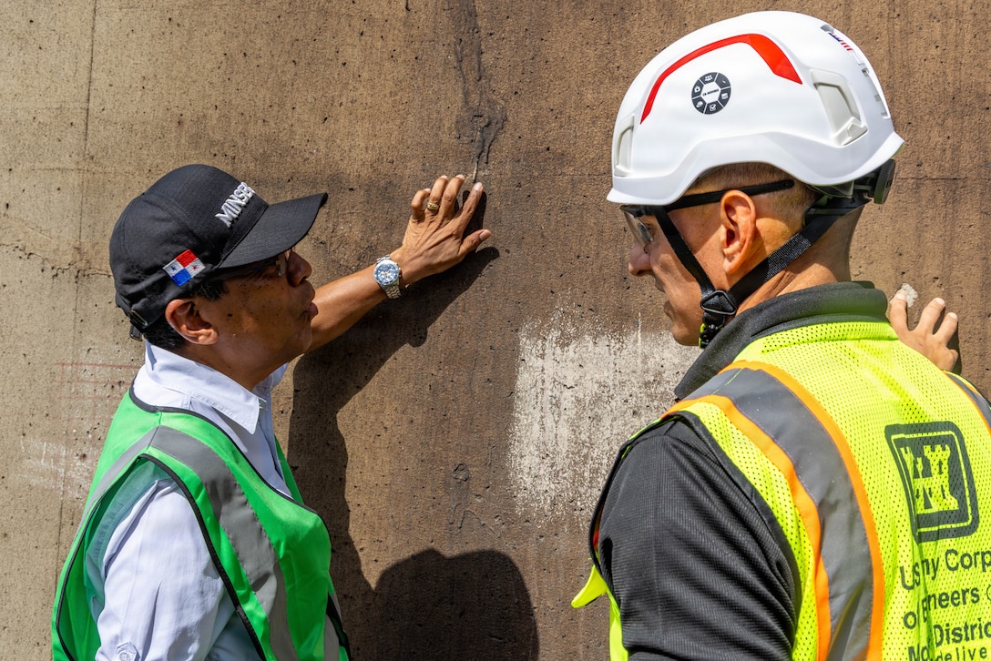 Two men touch a concrete structure while talking.