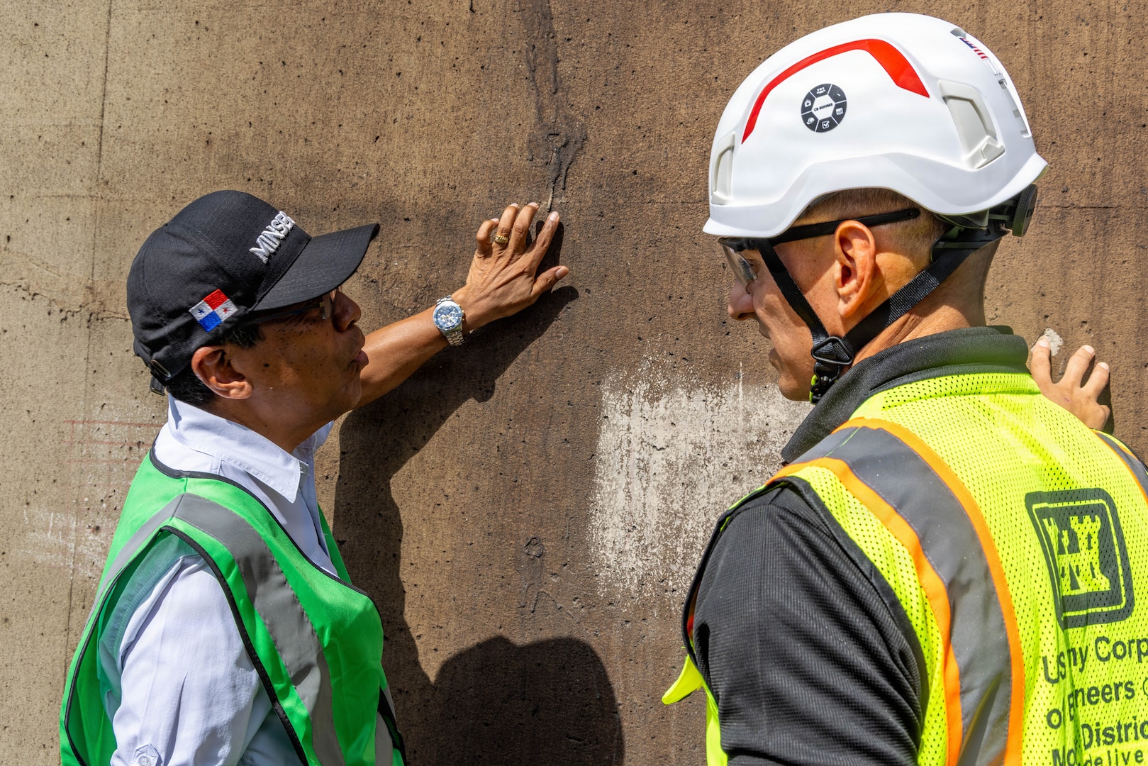 Two men touch a concrete structure while talking.