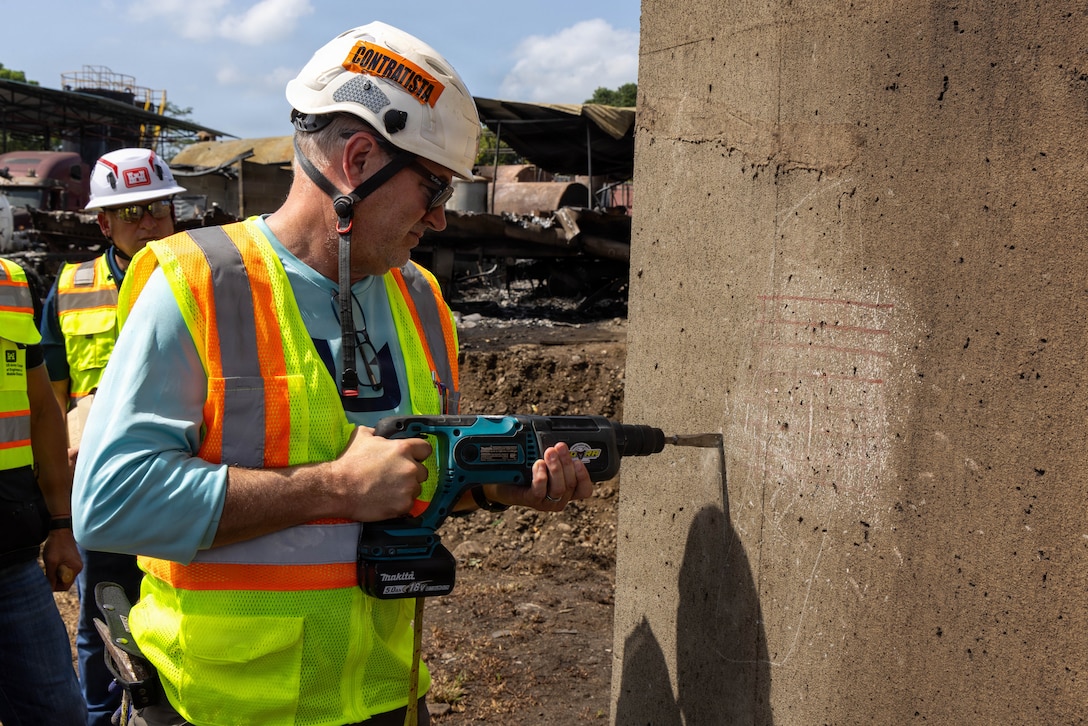 A man in a reflective vest and hard hat uses a drill on a concrete structure.