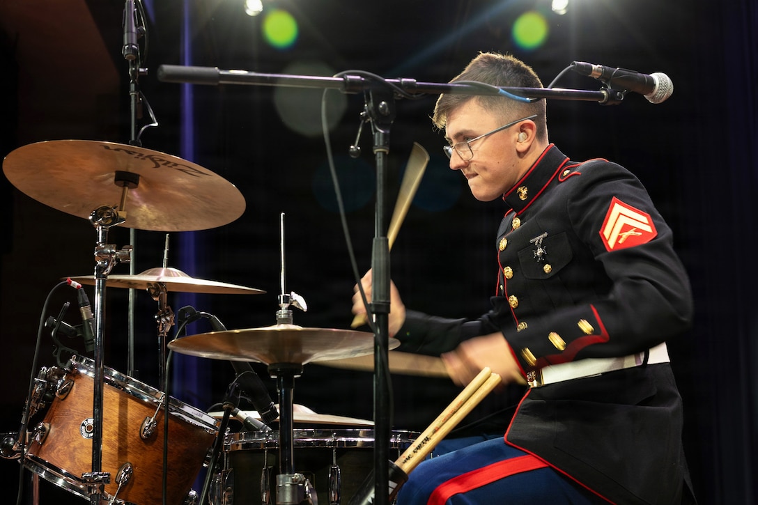 A Marine in ceremonial dress plays the drums in the dark under white spotlights.