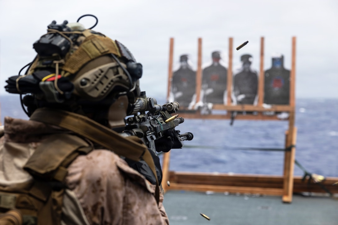 A person fires bullets on the deck of a ship toward four targets shaped like people that are attached to pieces of wood.
