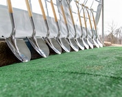 A row of shovels is seen lined up against a podium at an outdoor event.