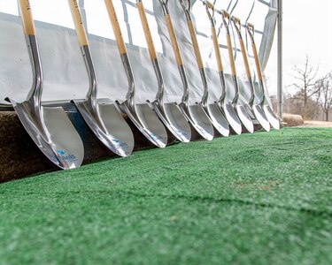A row of shovels is seen lined up against a podium at an outdoor event.