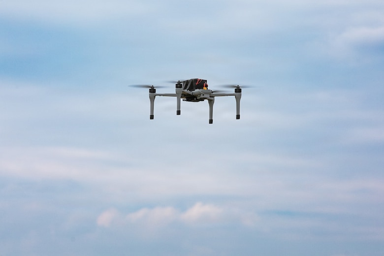 A drone flies in a blue sky with clouds.