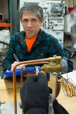 Donald Thompson, an air conditioning equipment mechanic with Pearl Harbor Naval Shipyard and Intermediate Maintenance Facility, observes another mechanic demonstrate how to adjust a refrigeration thermal expansion valve on a training device, Feb. 24, 2026. Thompson assesses mechanics to ensure they can troubleshoot and not just replace parts. PHNSY & IMF’s mission is to keep the Navy’s fleet “Fit to Fight” by repairing, maintaining, and modernizing the Navy's fast-attack submarines and surface ships. Strategically located in the heart of the Pacific, it is the most comprehensive fleet repair and maintenance facility between the U.S. West Coast and the Far East.