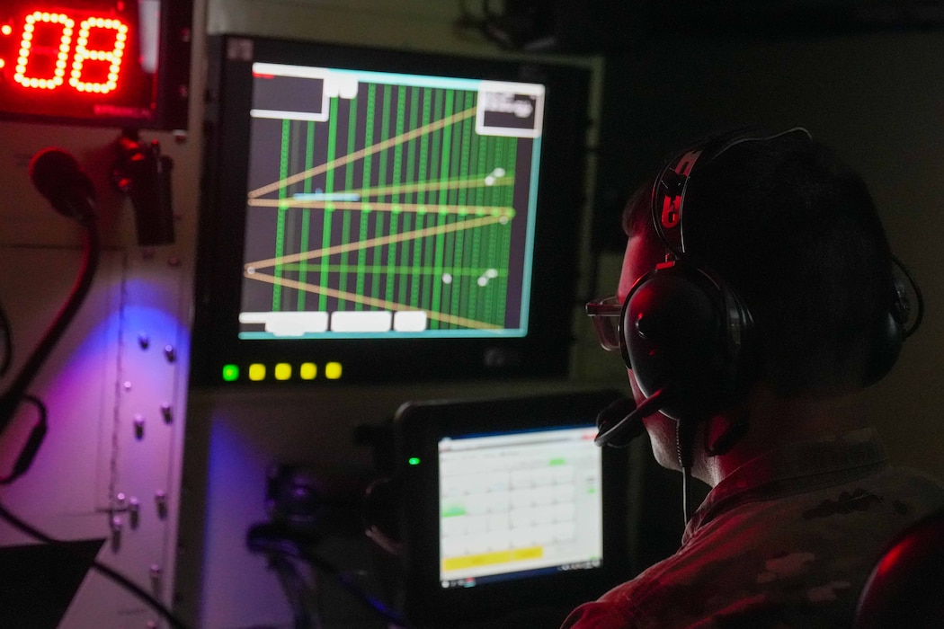 an air traffic controller wears a headset while looking at radar screens in a dark room