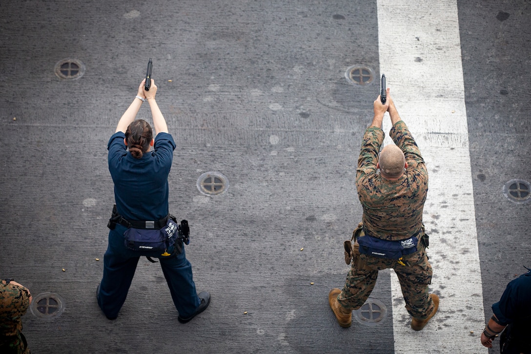 A U.S. Marine with 31st Marine Expeditionary Unit (MEU) and Sailor with America Expeditionary Strike Group fire at a target during a shooting competition aboard amphibious assault ship USS America (LHA 6) in the Solomon Sea, Aug. 7, 2021. The event consisted of Marines and Sailors competing as they shoot a series of drills with a goal of having the highest total score. The 31st MEU is operating aboard ships of the America Expeditionary Strike Group in the 7th fleet area of operation to enhance interoperability with allies and partners and serve as a ready response force to defend peace and stability in the Indo-Pacific region. (U.S. Marine Corps photo by Cpl. Karis Mattingly)