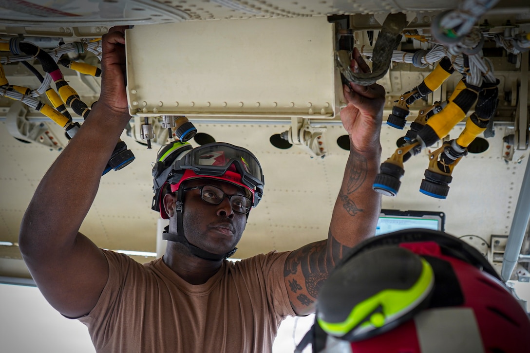 A sailor wearing a helmet raises their hands to work on the ceiling of an aircraft.