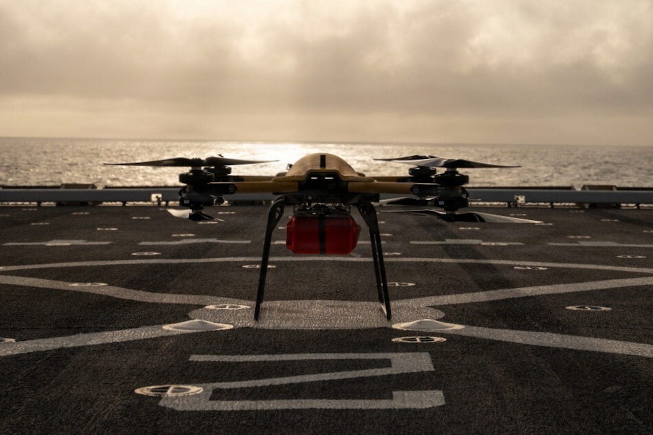 A drone sits on the deck of a military ship in the water.