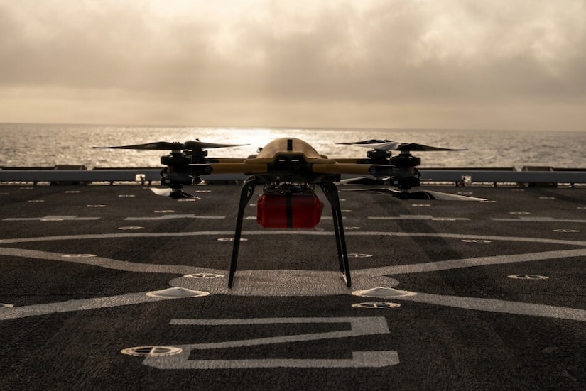 A drone sits on the deck of a military ship in the water.