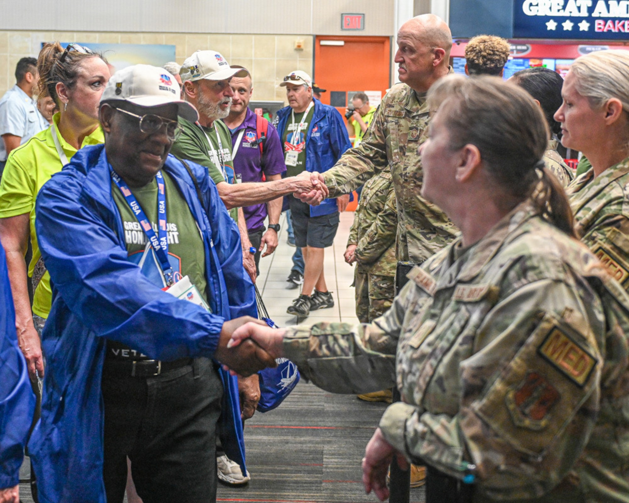 A Veteran wearing a blue jacket and a green shirt shakes hand with an Airman wearing a camouflage uniform.
