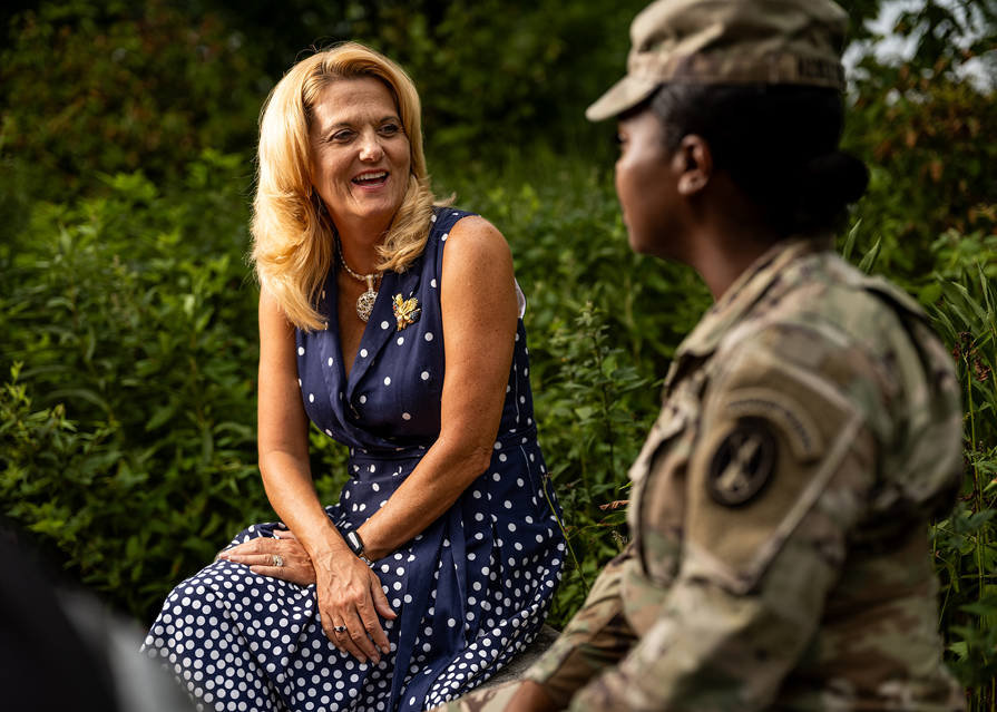 A woman seated facing the camera speaking to a uniformed service member.