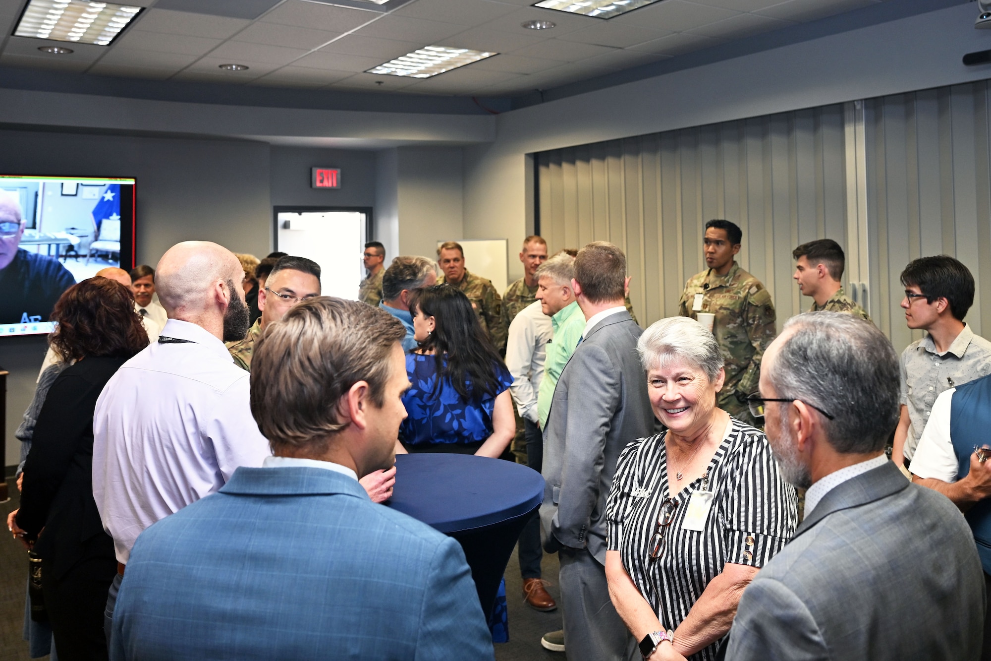 A group of men and women in civilian attire and military uniform mingle in a room