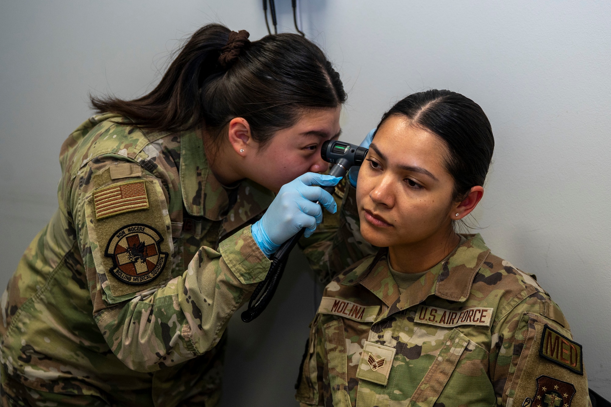 U.S. Air Force Senior Airman Yena Jung, left, occupational health technician with Bolling Medical Squadron Public Health, performs an ear inspection on Senior Airman Enmy Molina Martinez at Joint Base Anacostia-Bolling, Washington, D.C., April 8, 2026. The examination was just one of multiple, medical procedures given to Airmen prior to deployment for measuring physical and mental readiness. (U.S. Air Force photo by Senior Airman Shanel Toussaint)