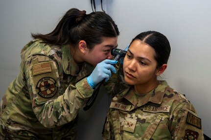 U.S. Air Force Senior Airman Yena Jung, left, occupational health technician with Bolling Medical Squadron Public Health, performs an ear inspection on Senior Airman Enmy Molina Martinez at Joint Base Anacostia-Bolling, Washington, D.C., April 8, 2026. The examination was just one of multiple, medical procedures given to Airmen prior to deployment for measuring physical and mental readiness. (U.S. Air Force photo by Senior Airman Shanel Toussaint)