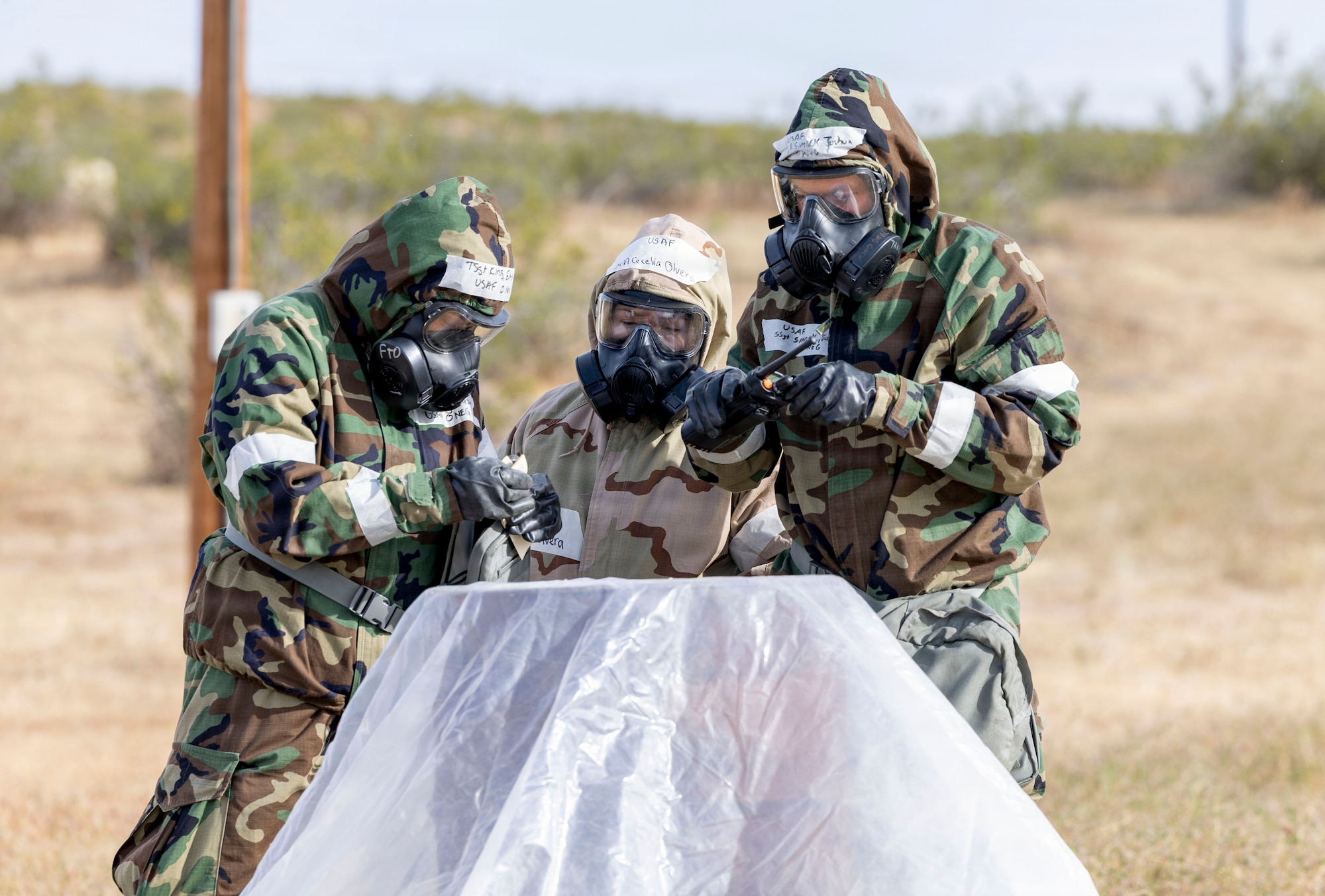 U.S. Air Force Tech. Sgt. Elyse King, left, installation personnel readiness noncommisioned officer in charge, 412th Force Support Squadron, Senior Airman Cecelia Olvera, middle, 412th Operations Group, and Staff Sgt. Joshua Simock, 912th Aircraft Maintenance Squadron, observe simulated M9 chemical detection tape as part of a chemical, biological, radiological, and nuclear threats defense validation exercise at Edwards Air Force Base, California, March 30, 2026. The 812th Civil Engineer Squadron's Office of Emergency Management validated more than 250 Airmen over a three-day period in late March. (U.S. Air Force photo by Jennifer Healy)