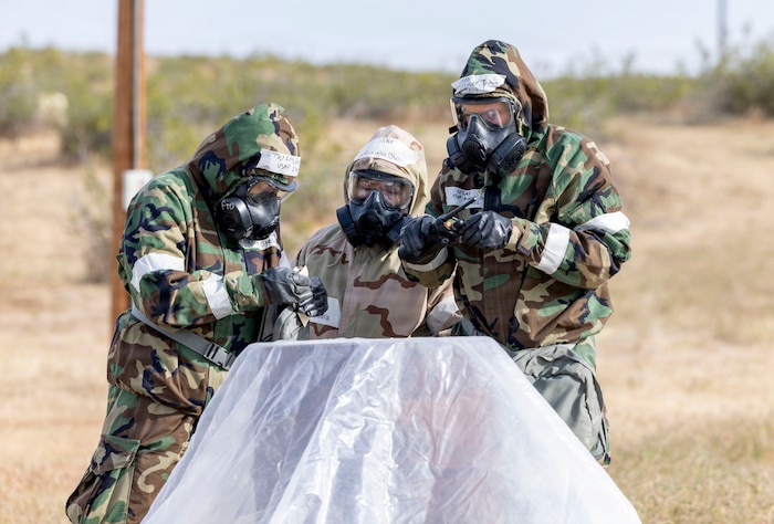 U.S. Air Force Tech. Sgt. Elyse King, left, installation personnel readiness noncommisioned officer in charge, 412th Force Support Squadron, Senior Airman Cecelia Olvera, middle, 412th Operations Group, and Staff Sgt. Joshua Simock, 912th Aircraft Maintenance Squadron, observe simulated M9 chemical detection tape as part of a chemical, biological, radiological, and nuclear threats defense validation exercise at Edwards Air Force Base, California, March 30, 2026. The 812th Civil Engineer Squadron's Office of Emergency Management validated more than 250 Airmen over a three-day period in late March. (U.S. Air Force photo by Jennifer Healy)