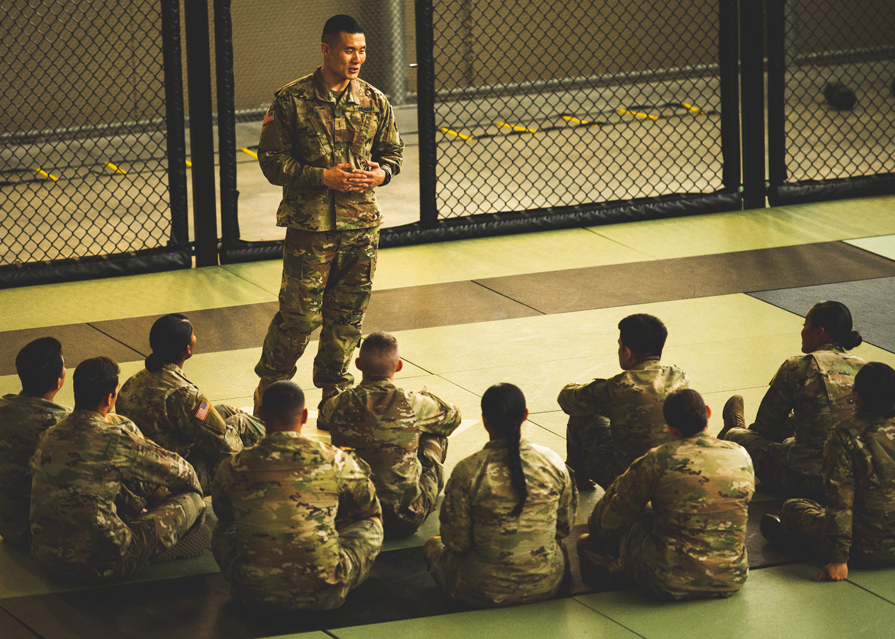 A uniformed service member standing up in front of a group of seated uniformed personnel