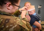 Medical professional in uniform uses a tape measure on a baby's head while a woman holds the baby.