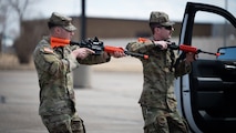 Two soldiers wielding training rifles approach a vehicle during a training exercise.