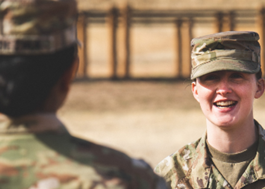 Two uniformed service members speaking. One is facing the camera and smiling